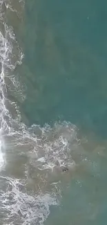 Aerial view of teal ocean waves with white sea foam on a beach.