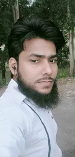 Man with beard in a nature setting, wearing earphones.