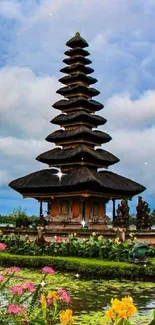 Tranquil pagoda by a lake with vibrant flowers and blue sky.