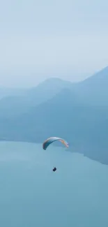 Paraglider gliding over calm, blue waters and mountains.