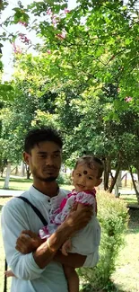 Father with child in a lush green park, surrounded by trees.