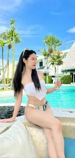 Woman sits by serene poolside, enjoying a sunny day with vibrant blue skies.