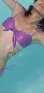 Woman relaxing in pool wearing a purple swimsuit.