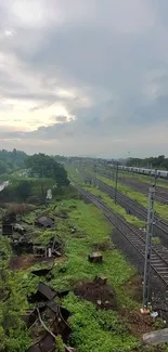 Scenic view of railway tracks beneath an overcast sky, surrounded by greenery.