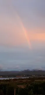 Rainbow over mountains with pastel sky.