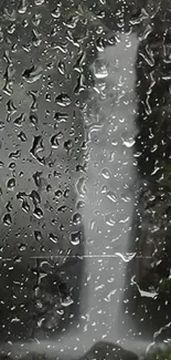 Rainy window view of a waterfall in a lush forest.