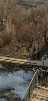 Serene river flowing under a bridge with brown foliage and mountains.