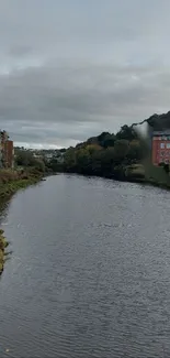 Serene river with cityscape and overcast sky.