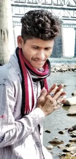 Person standing by a river with a bridge in the background.