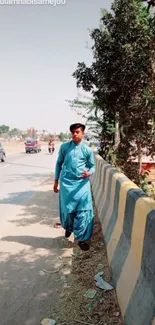 Man in blue walks along a roadside under trees.