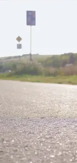 Sunlit road with blue sky and green fields, ideal mobile wallpaper.