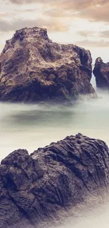 Serene rock formations by misty ocean waves at sunset.