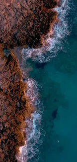 Aerial view of rocky coastline meeting deep teal blue ocean waves.