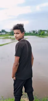 Young man gazing at a serene landscape with water and fields.