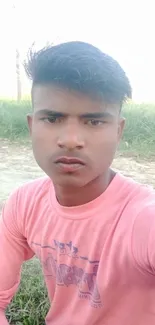 Young individual in a serene rural setting with pink shirt against a field backdrop.