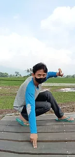 Man near tree in green rural landscape with cloudy sky.