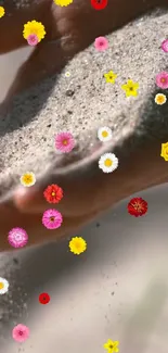 Hands holding sand with colorful flowers cascading down.