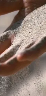 Hand letting soft sand flow gently through fingers in nature.