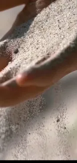 Hand gently allowing sand to flow through fingers.