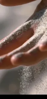 Close-up of hand sifting soft sand in a serene, minimalist design wallpaper.