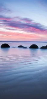 Serene beach scene with pink sunset and spherical rocks on the shore.