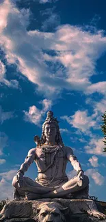 Shiva statue meditating beneath a blue sky with clouds and greenery.