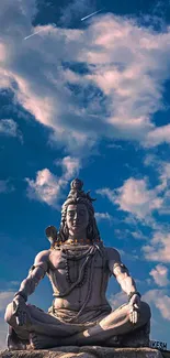 Statue of Shiva against a blue sky with fluffy clouds in the background.