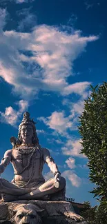 Shiva statue with blue sky background and fluffy clouds.