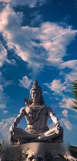 Shiva statue meditating beneath a vibrant blue sky with clouds.