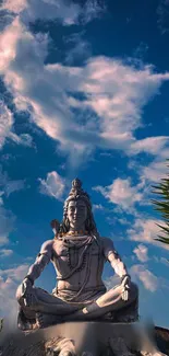 Statue of Shiva meditating under a clear blue sky with clouds.