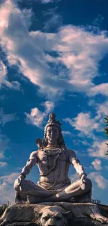 Statue of Shiva against a vibrant blue sky with clouds.