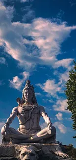 Shiva statue against a vibrant blue sky with fluffy clouds.