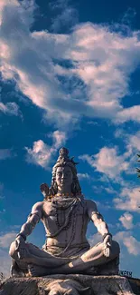 Statue of Lord Shiva meditating under a bright blue sky with clouds.