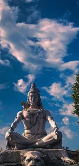 Majestic Shiva statue under a blue, cloud-filled sky.