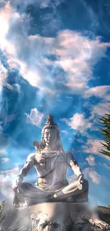 Shiva statue against a blue and cloudy sky in peaceful meditation.