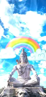 Shiva statue with rainbow and clouds under a bright blue sky.