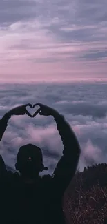 Silhouette and heart shape against pink sky and clouds on mobile wallpaper.