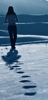 A lone figure walks through snowy mountains under a clear blue sky.