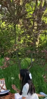 Girl enjoying a picnic under a blossoming tree with lush greenery.