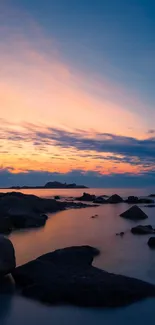 Tranquil sunset beach wallpaper with rocky shoreline and colorful twilight sky.