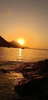 Sunset over a peaceful beach with golden hues and silhouettes of hills.