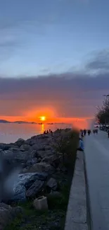 Vibrant sunset over the sea with rocky shore and a serene pathway.