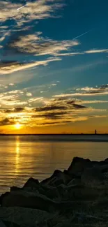 Serene sunset over ocean with rocky shore and golden sky.