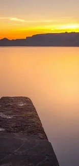 A tranquil sunset view over the ocean with a glowing orange sky and horizon.