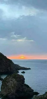 Serene sunset with ocean and rocky cliffs in the foreground.