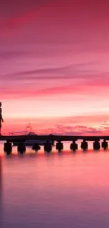 Silhouette on dock with pink sunset sky reflecting on water.