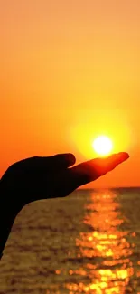 Hand holding the sun at sunset over a calm ocean.