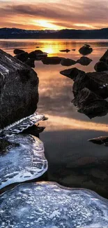 Sunset reflecting over icy rocks by a serene lakeshore.