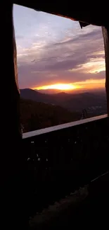 Sunset over mountains seen through a wooden window, creating a serene view.