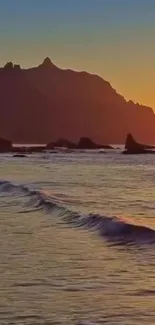 A serene sunset over the ocean with gentle waves and a mountain backdrop.